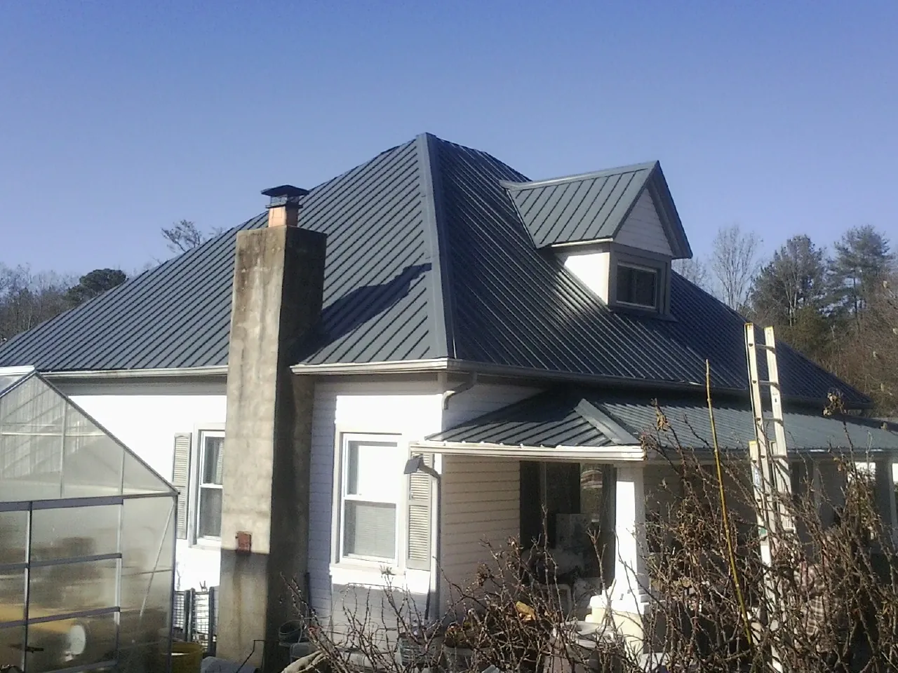Dark blue standing seam metal roof on a white farmhouse with dormer — Slate & Tile Roof Repair by Roofing Brothers in Stapleton