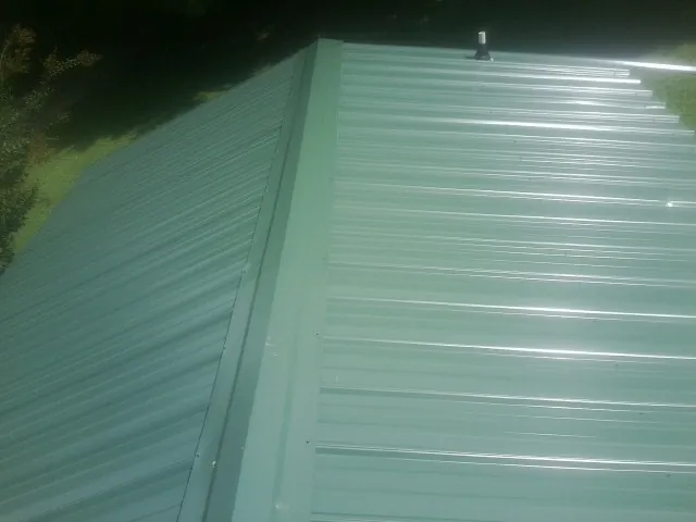 New green metal panels meeting at the ridge of a roof — Flat Roof Repair work by our crew in Stapleton