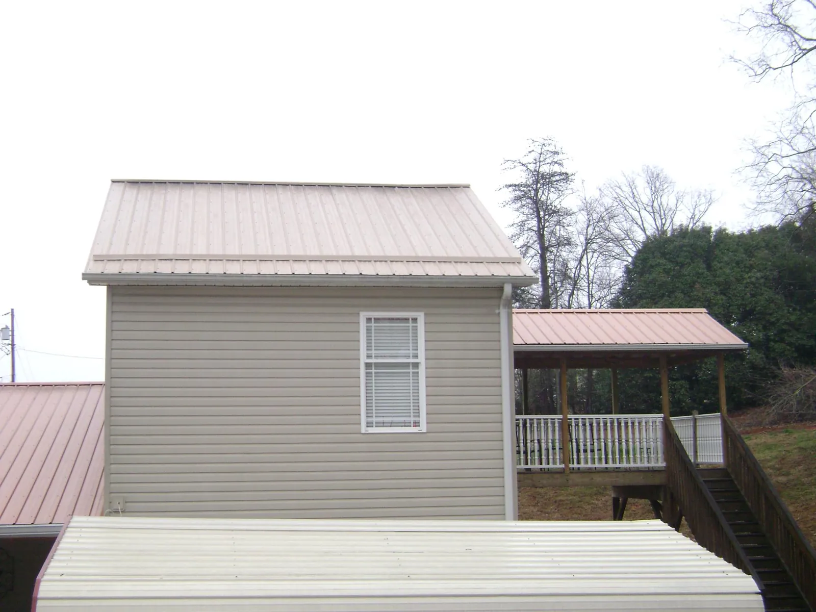 Tan metal roofs on a two story addition and attached porch, from a Roof Replacement job in Stapleton